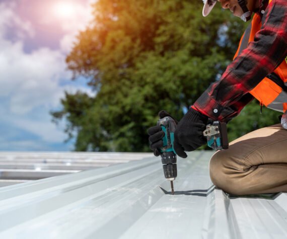 Worker with roofer tools wearing protective gear installing new roof on top roof at construction site,metal roof.